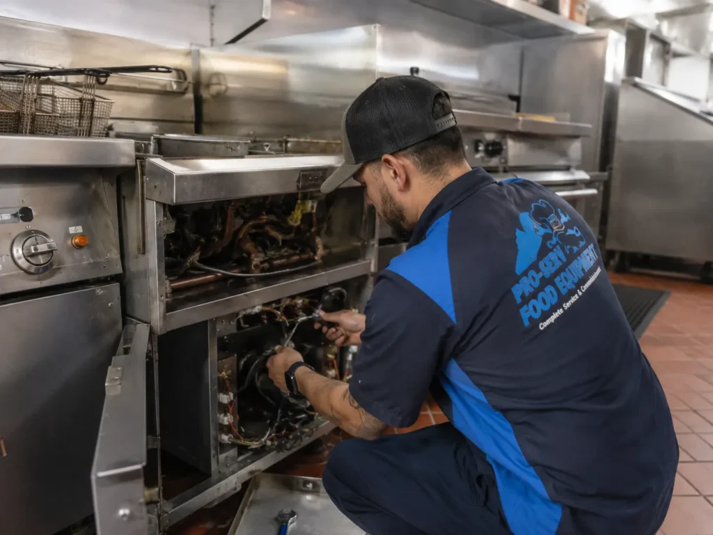 Pro-Serv Food Equipment technician repairing a commercial deep fryer in a professional restaurant kitchen